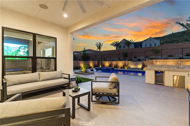 patio terrace at dusk featuring an outdoor living space, a fenced backyard, area for grilling, a ceiling fan, and a sink