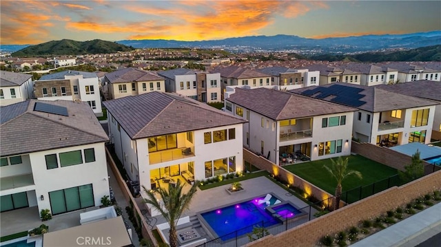 back of house at dusk featuring stucco siding, a residential view, a fenced backyard, and a pool with connected hot tub