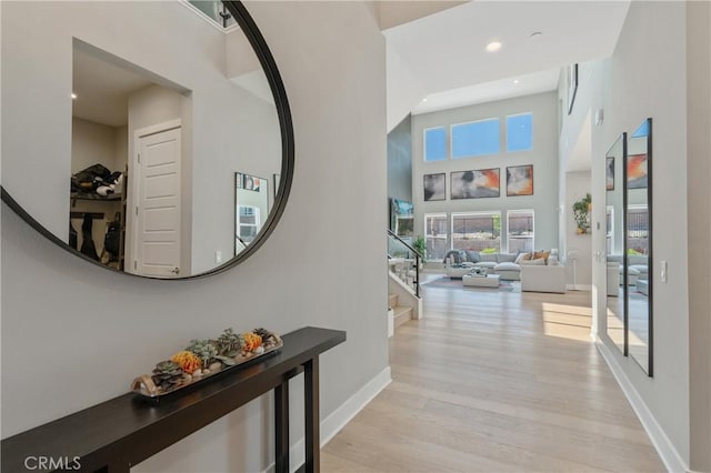 corridor with stairway, baseboards, light wood-type flooring, recessed lighting, and a towering ceiling