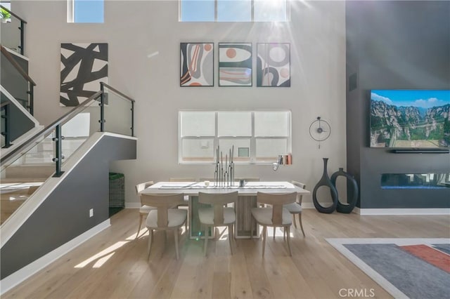 dining room featuring a high ceiling, wood finished floors, baseboards, and stairs
