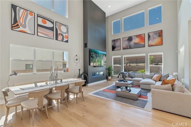 living room with a high ceiling, light wood-style floors, and baseboards