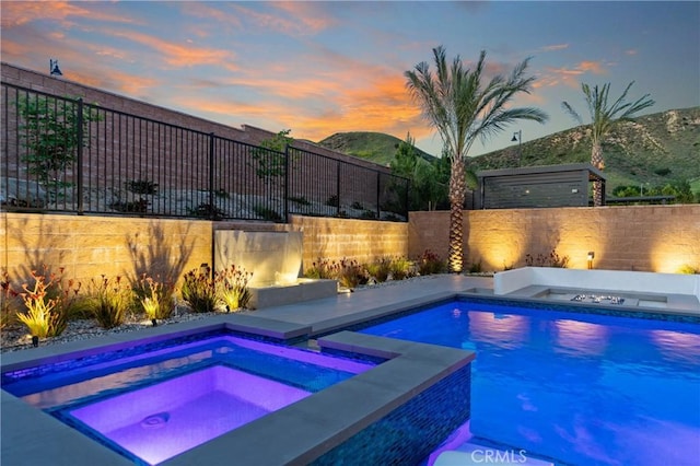 pool at dusk featuring an in-ground hot tub and a fenced backyard