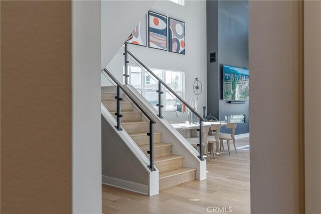 stairway with wood finished floors, baseboards, and a towering ceiling
