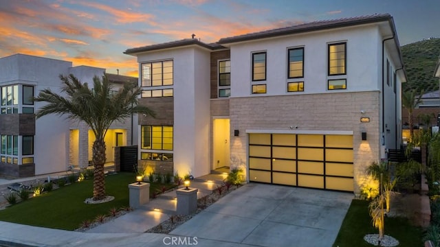 contemporary house with an attached garage, driveway, stone siding, stucco siding, and a yard