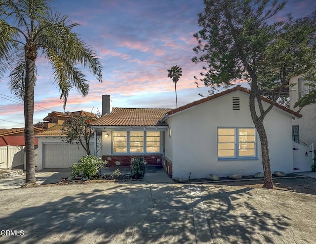 view of front of property featuring a tile roof, a chimney, stucco siding, and an attached garage