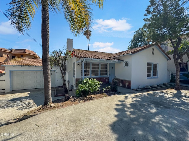 mediterranean / spanish-style home featuring concrete driveway, a tile roof, stucco siding, and a chimney