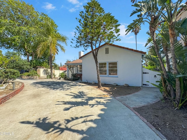 view of home's exterior featuring stucco siding, fence, a gate, a chimney, and a tile roof