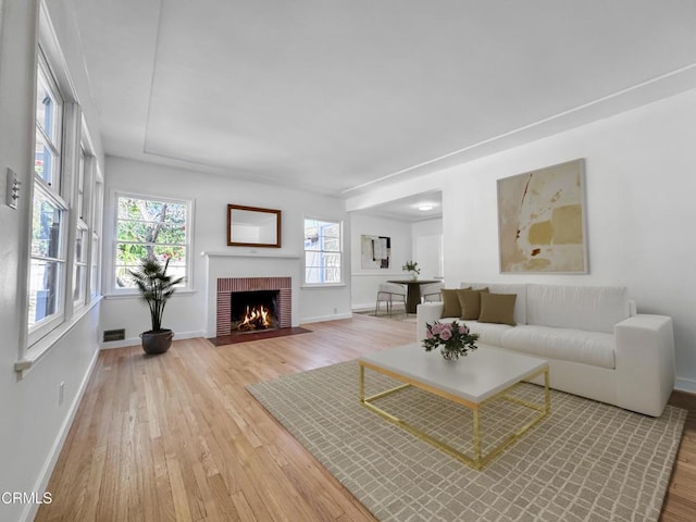 living room featuring light wood-style flooring, baseboards, and a brick fireplace