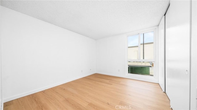 unfurnished room featuring light wood-type flooring, baseboards, and a textured ceiling