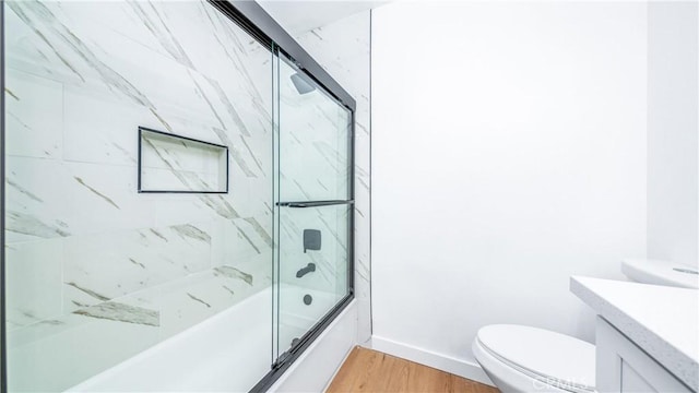full bath with wood finished floors, toilet, vanity, baseboards, and shower / bath combination with glass door