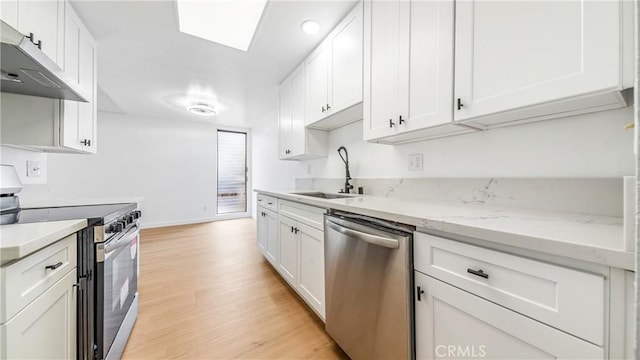 kitchen with appliances with stainless steel finishes, a sink, under cabinet range hood, light wood finished floors, and white cabinets
