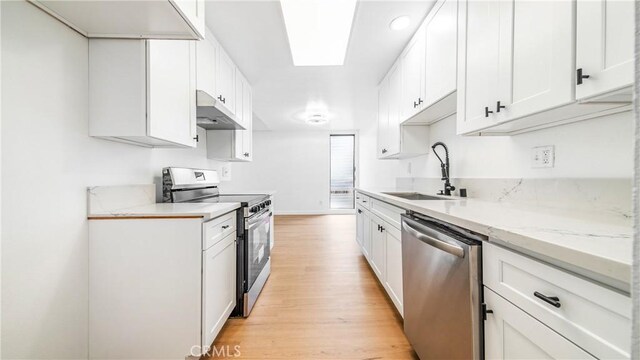 kitchen with appliances with stainless steel finishes, under cabinet range hood, a sink, light wood-style flooring, and white cabinetry