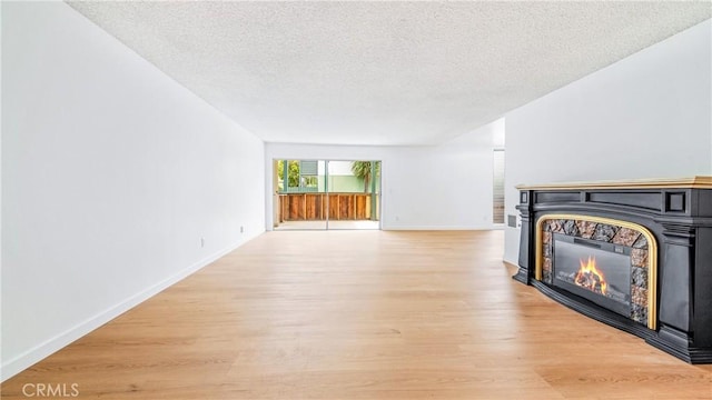 unfurnished living room with a textured ceiling, a glass covered fireplace, light wood-style floors, and baseboards