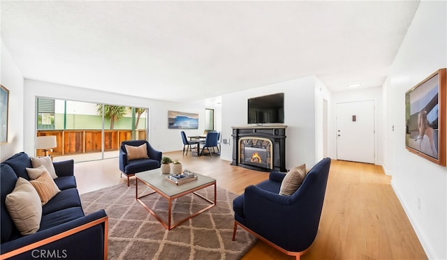 living room with light wood finished floors, a glass covered fireplace, and baseboards