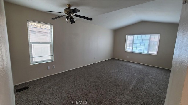 empty room with vaulted ceiling, dark colored carpet, and ceiling fan