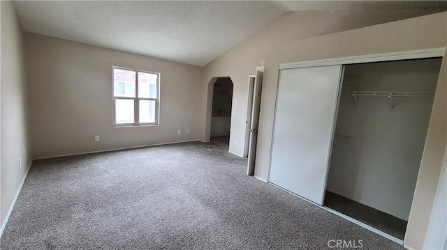 unfurnished bedroom featuring vaulted ceiling, arched walkways, carpet flooring, a closet, and baseboards
