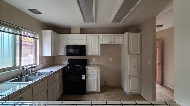 kitchen featuring tile counters, black appliances, a sink, and white cabinets
