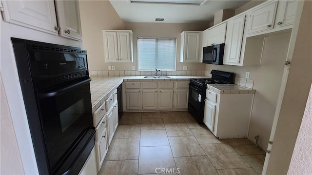 kitchen featuring black appliances, tile counters, a sink, white cabinets, and light tile patterned floors