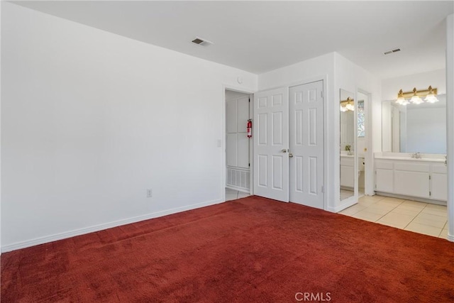 unfurnished bedroom with light colored carpet, a sink, baseboards, ensuite bath, and light tile patterned flooring