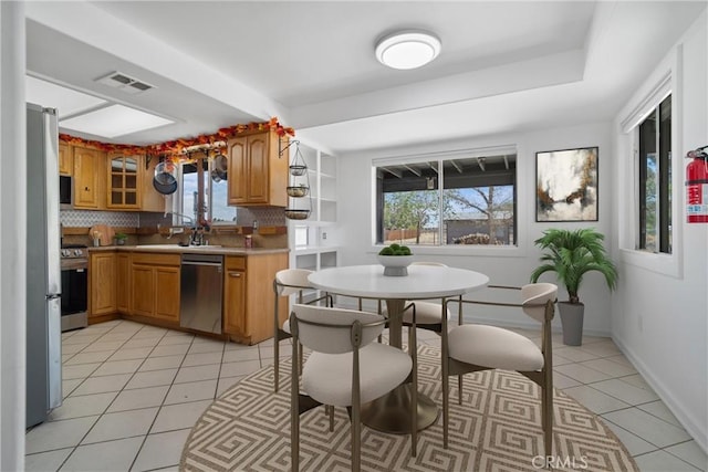 kitchen featuring stainless steel appliances, tasteful backsplash, light tile patterned floors, brown cabinetry, and light countertops