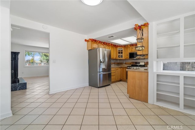 kitchen with appliances with stainless steel finishes, a wood stove, baseboards, light tile patterned flooring, and tasteful backsplash