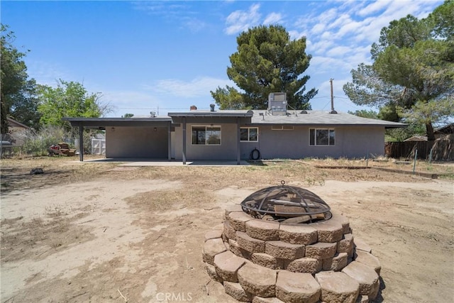 back of property featuring a fire pit, an attached carport, stucco siding, and fence