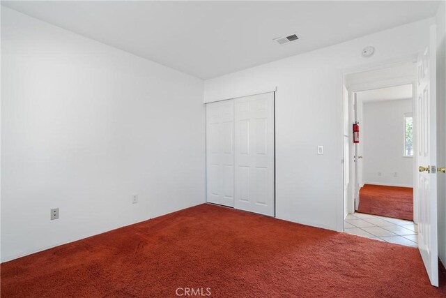 unfurnished bedroom with carpet floors, a closet, and tile patterned flooring