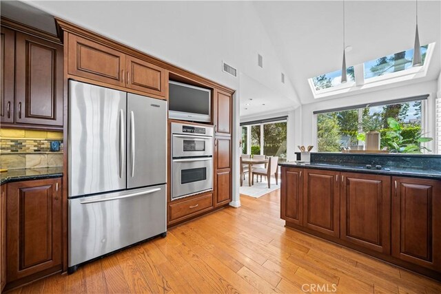 kitchen with appliances with stainless steel finishes, a skylight, light wood-style flooring, high vaulted ceiling, and backsplash