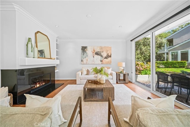 living room featuring wood finished floors, a glass covered fireplace, ornamental molding, and recessed lighting