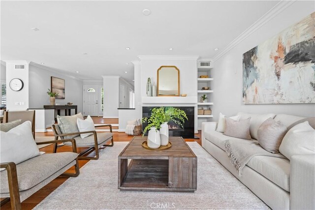 living room with crown molding, recessed lighting, light wood-style flooring, and a warm lit fireplace