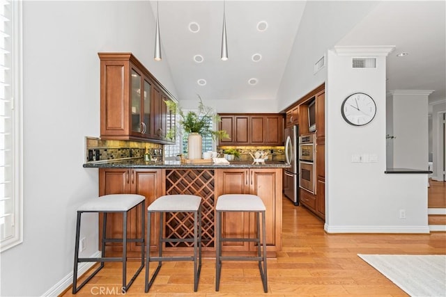kitchen featuring appliances with stainless steel finishes, a peninsula, tasteful backsplash, glass insert cabinets, and vaulted ceiling