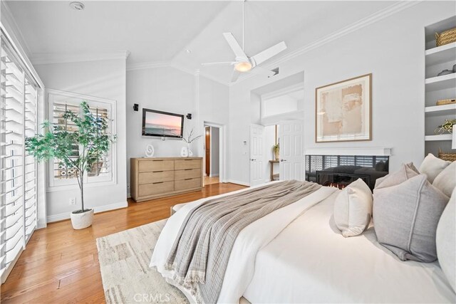 bedroom featuring ornamental molding, lofted ceiling, wood finished floors, baseboards, and a lit fireplace