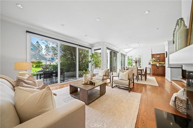 living area with healthy amount of natural light, light wood-type flooring, crown molding, and recessed lighting