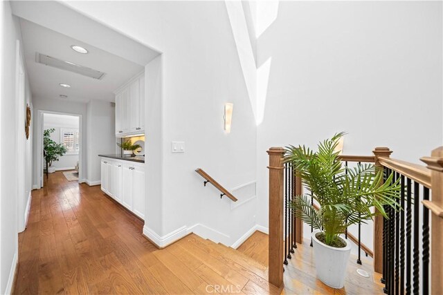 hallway with an upstairs landing, light wood-style floors, baseboards, and recessed lighting