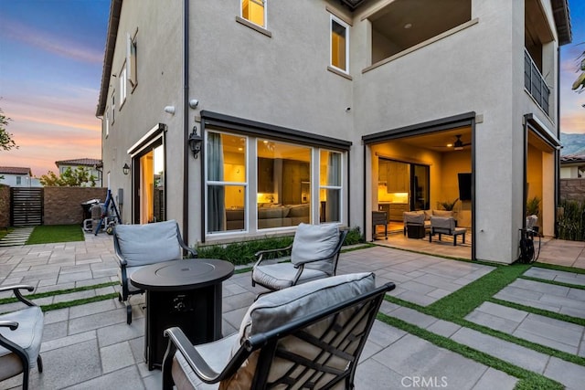 back of house at dusk featuring a patio area, stucco siding, an outdoor living space with a fire pit, and fence