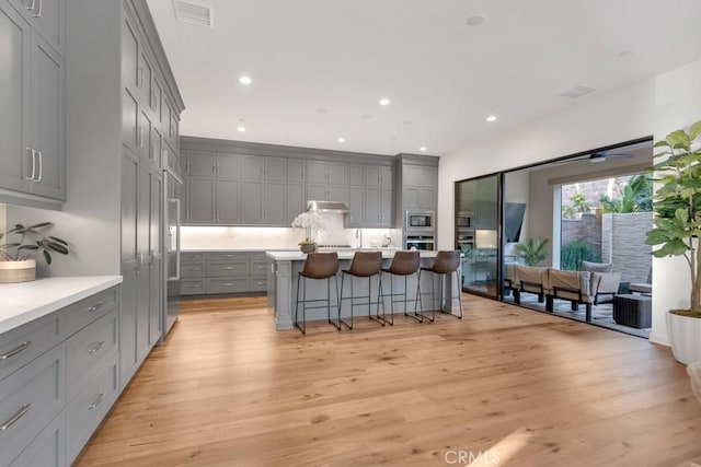 kitchen featuring gray cabinetry, appliances with stainless steel finishes, a kitchen bar, light wood-type flooring, and light countertops