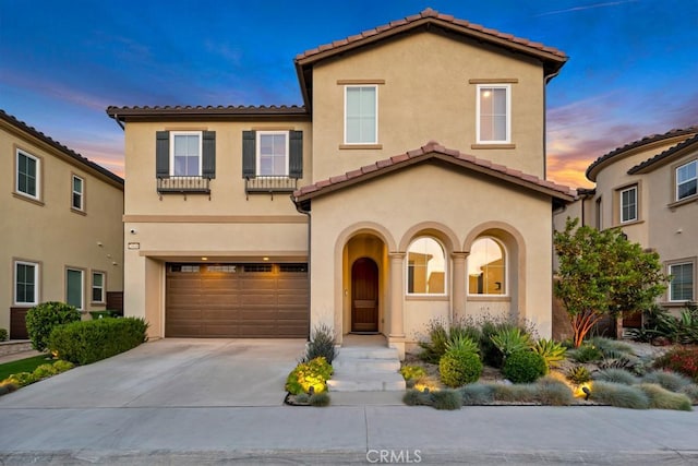 mediterranean / spanish-style home featuring a tiled roof, stucco siding, a garage, and concrete driveway