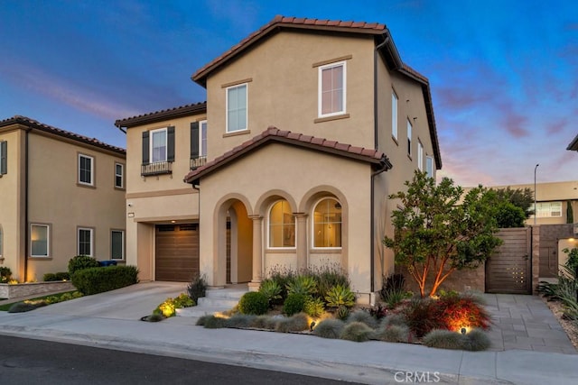 mediterranean / spanish-style house with a tiled roof, a garage, a gate, and stucco siding