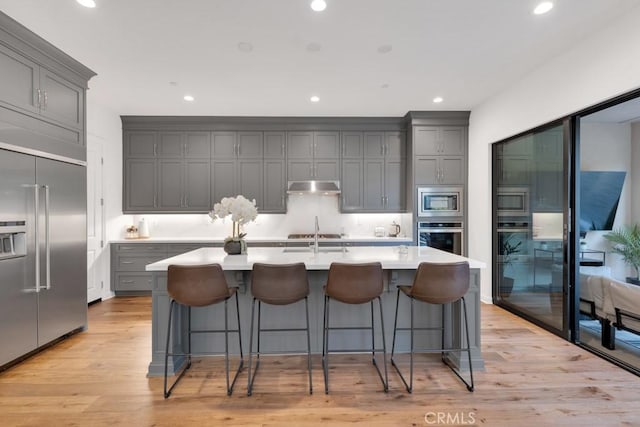 kitchen featuring built in appliances, gray cabinets, under cabinet range hood, light wood-type flooring, and light countertops