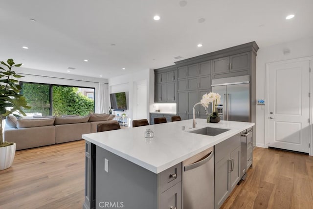 kitchen featuring a sink, gray cabinets, appliances with stainless steel finishes, an island with sink, and open floor plan