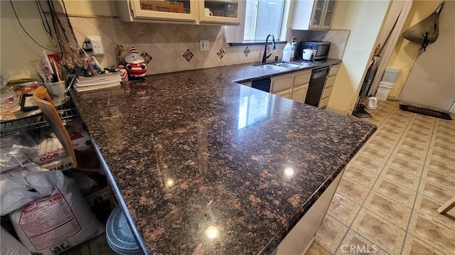 kitchen with a sink, dishwasher, glass insert cabinets, a peninsula, and backsplash