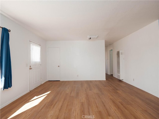 empty room featuring a heating unit, light wood-style floors, and baseboards