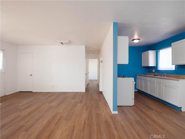 kitchen with open floor plan, light wood finished floors, a sink, white cabinets, and baseboards