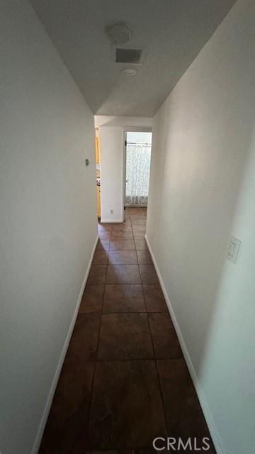 hall featuring baseboards and dark tile patterned flooring