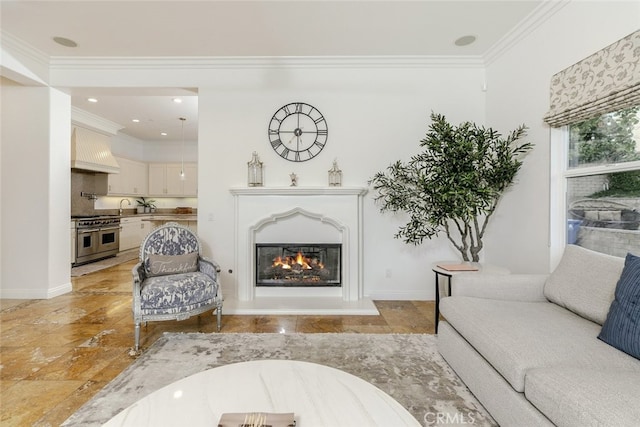 living room with stone tile flooring, ornamental molding, baseboards, recessed lighting, and a glass covered fireplace