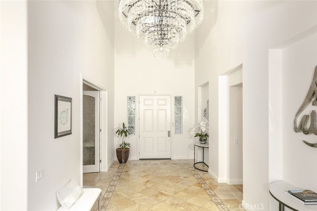 foyer with a chandelier, a towering ceiling, inlaid floor details, and baseboards
