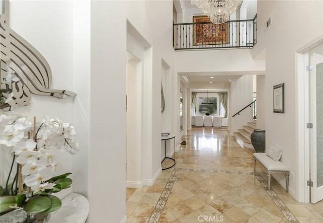entryway featuring inlaid floor details, stairs, baseboards, a chandelier, and a towering ceiling