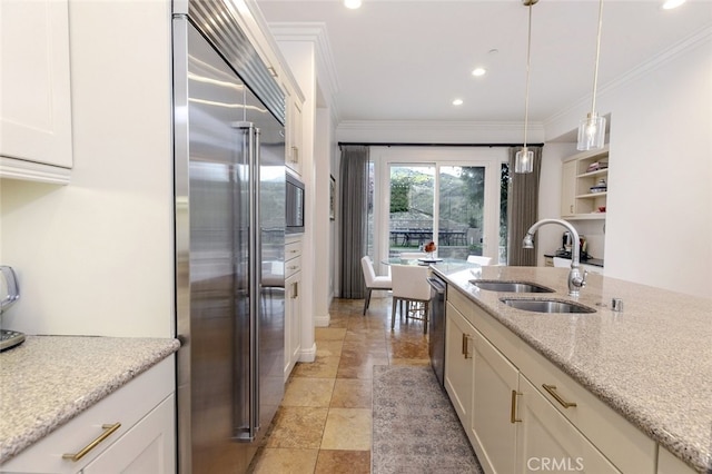 kitchen featuring built in appliances, a sink, white cabinets, ornamental molding, and hanging light fixtures
