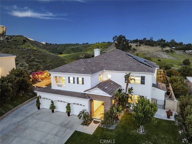 view of front of home featuring a garage, driveway, solar panels, a chimney, and a front yard