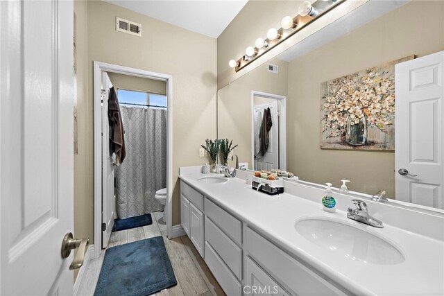 bathroom with toilet, double vanity, and wood finished floors